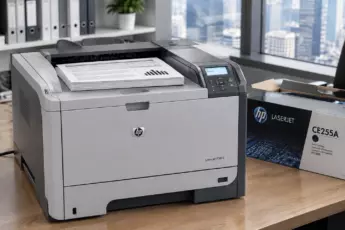 Монохромный лазерный принтер HP LaserJet P3015 с распечатанными документами и картриджем CE255A на офисном столе